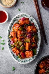 platter with chili paneer surrounded by chopsticks, sauce, and sesame seeds