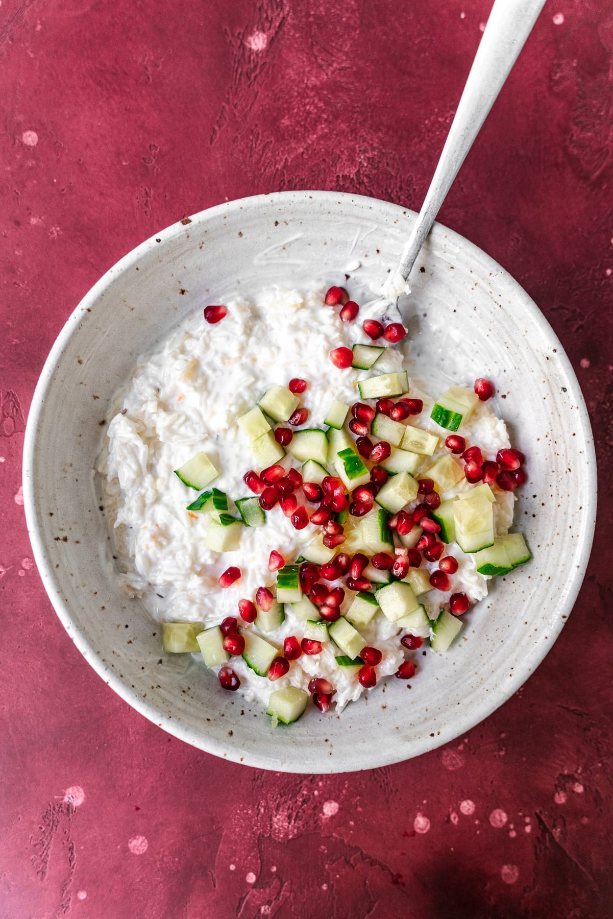 a bowl of rice filled with curd and chopped cucumbers with pomegranates