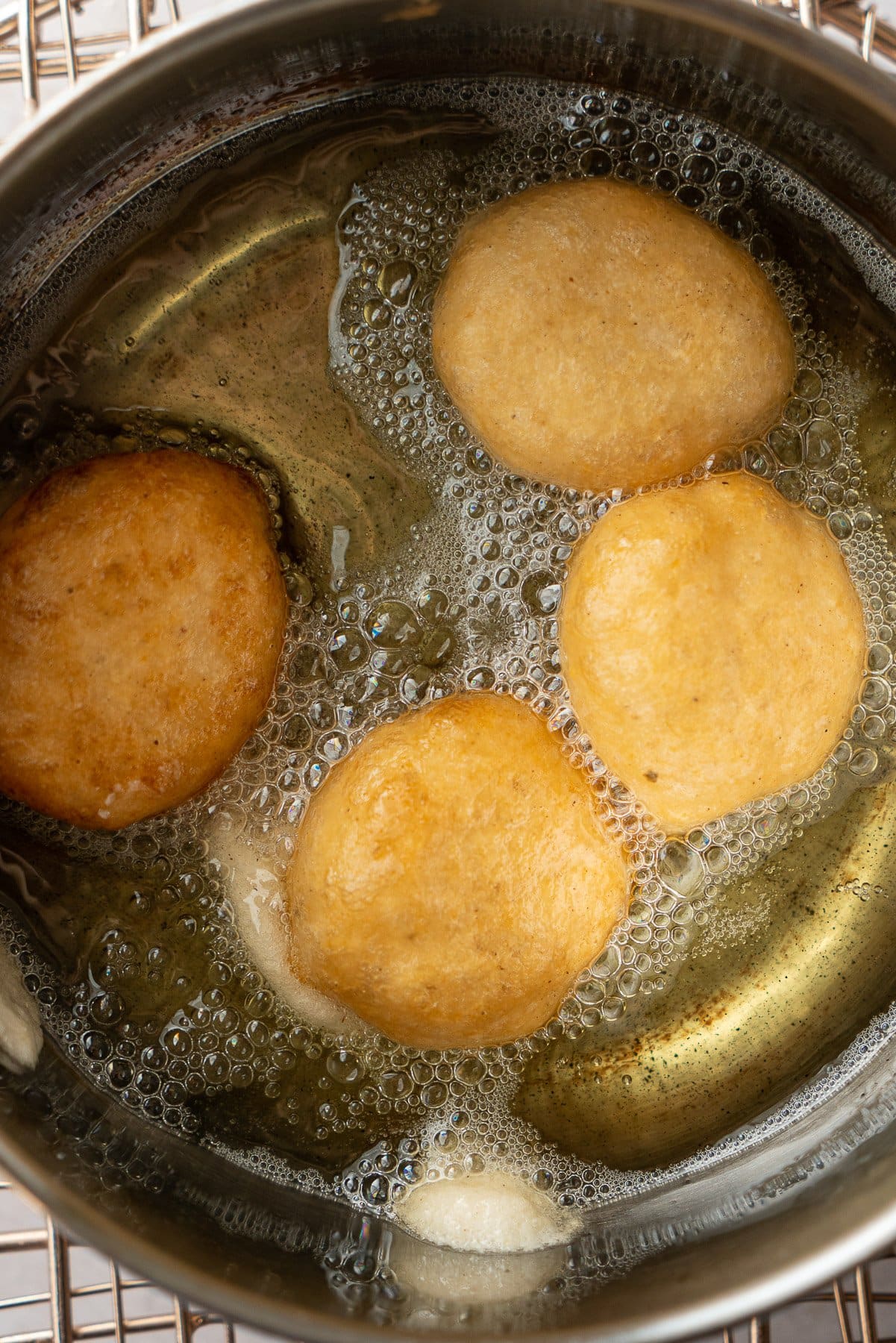 four golden brown vadas frying in a metal pot with oil