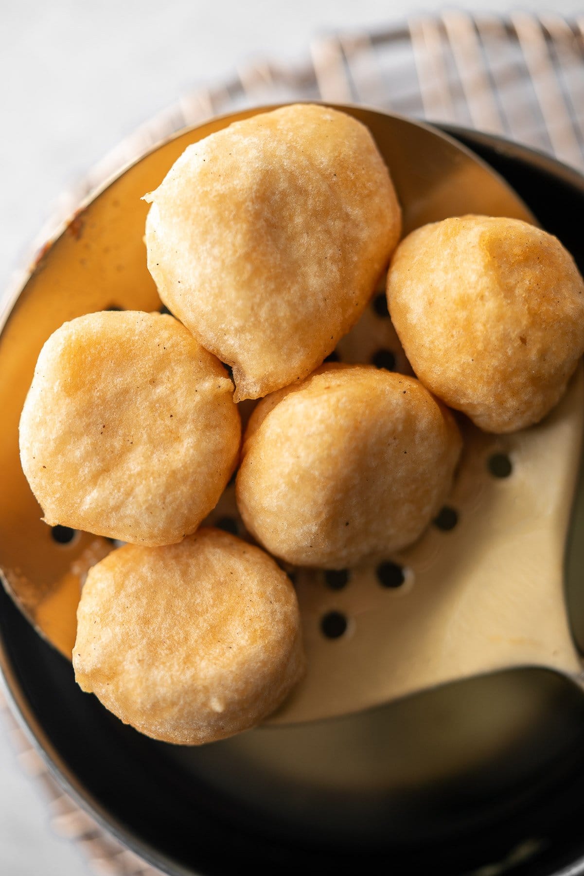 five lightly golden brown dahi vadas in a slotted spoon