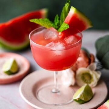 fresh homemade watermelon juice in a coupe with lime, fresh watermelon, and mint