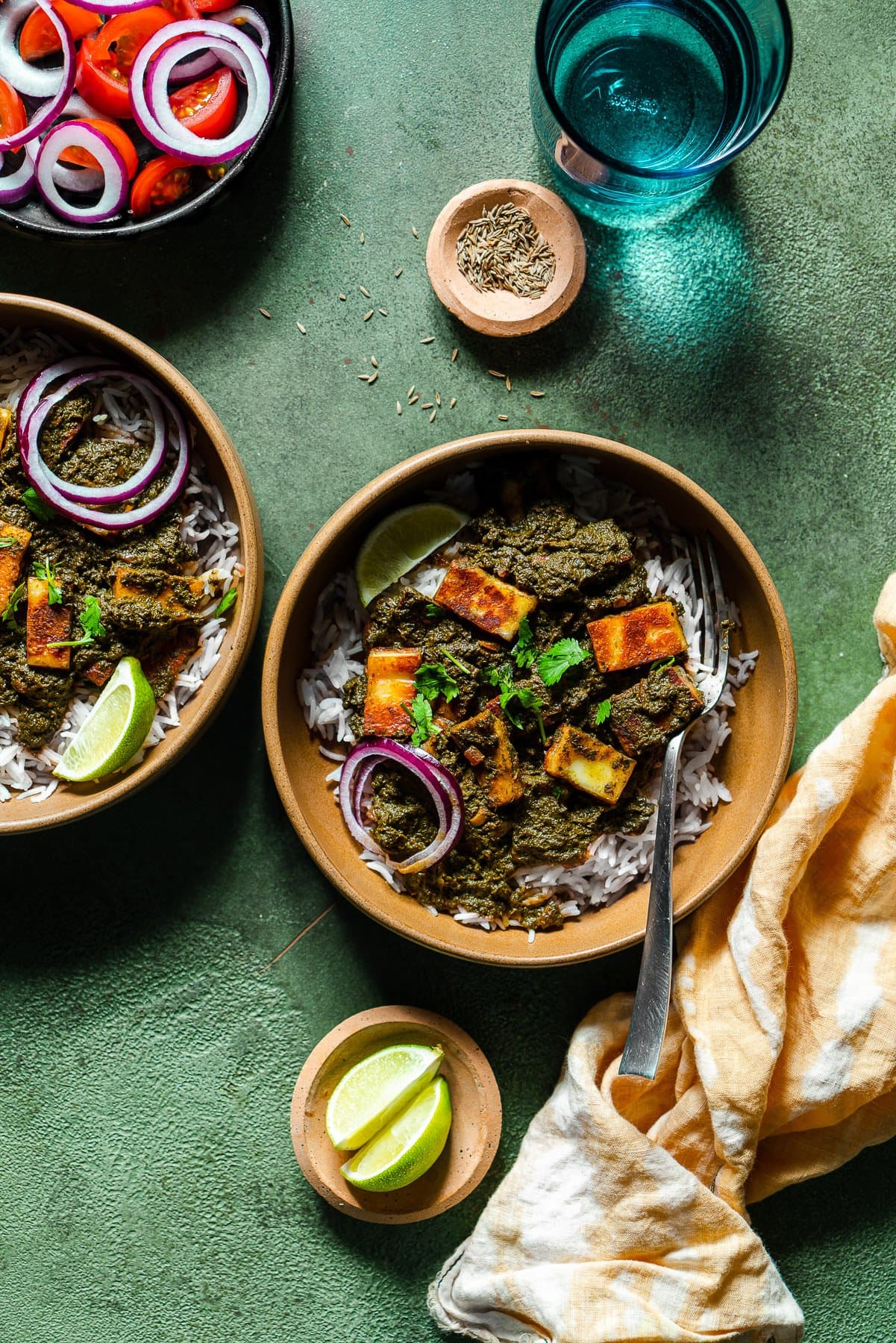 two bowls of swiss chard saag paneer with limes and a tomato onion salad