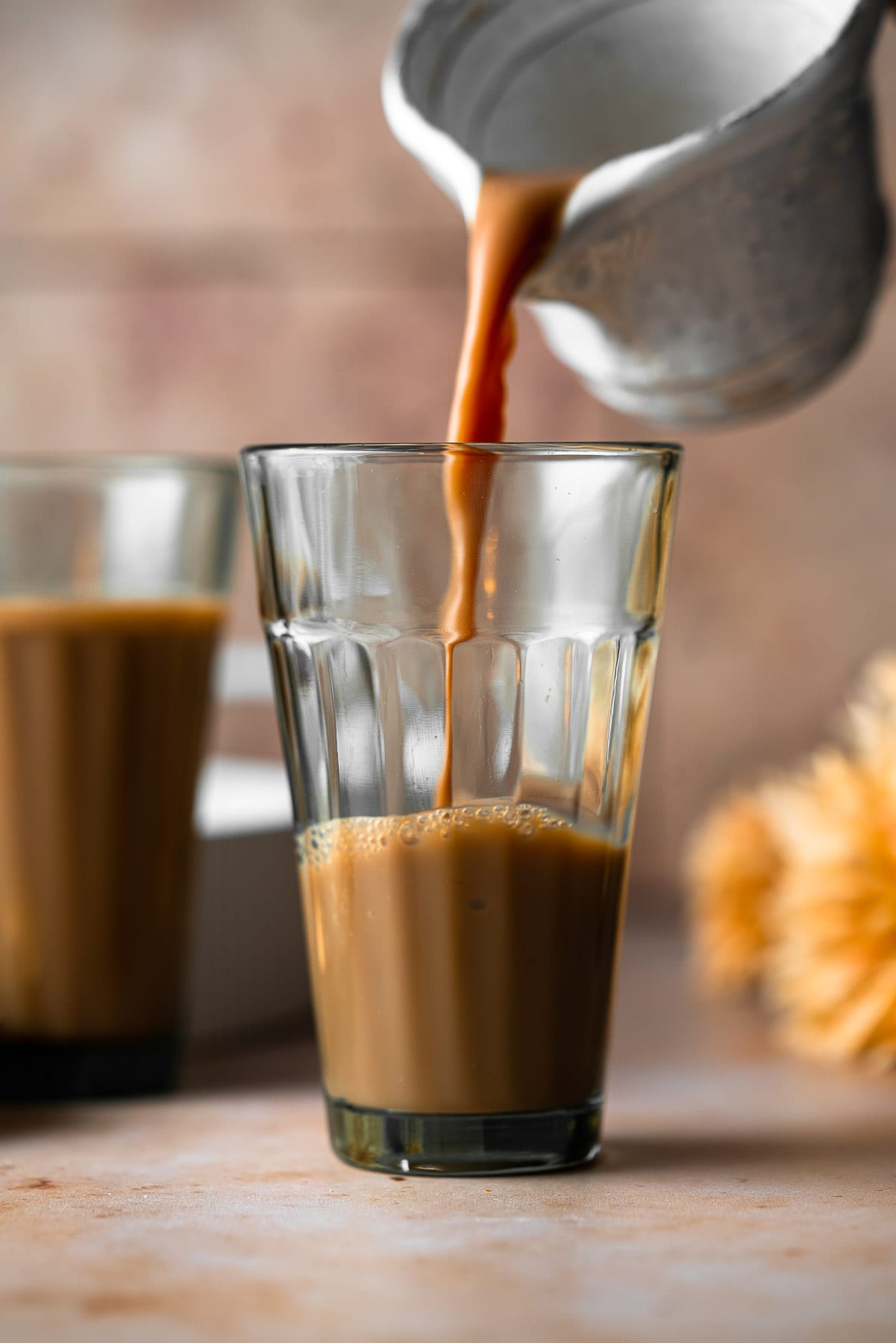 pouring adrak chai from a small pitcher into a glass cup