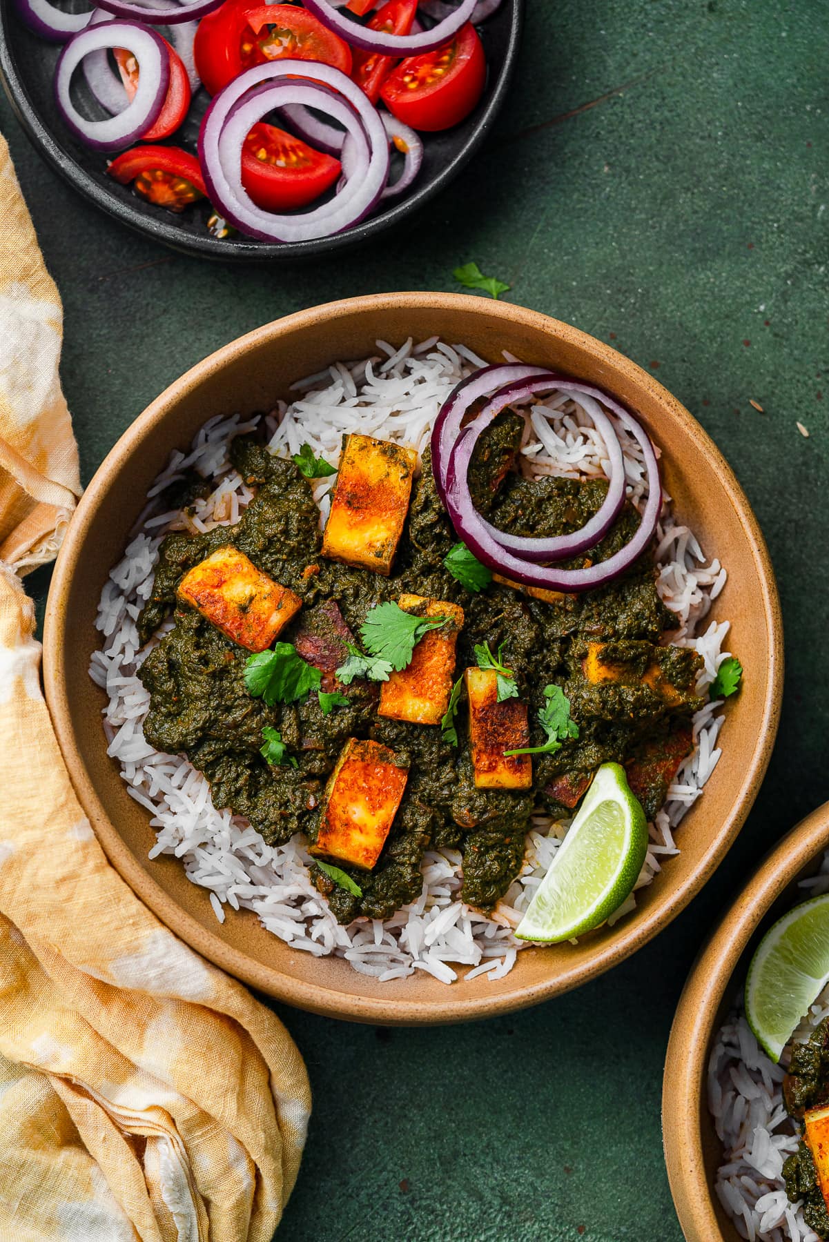 a bowl of swiss chard saag paneer with tomato onion salad