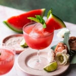 fresh homemade watermelon juice in a coupe with lime, fresh watermelon, and mint