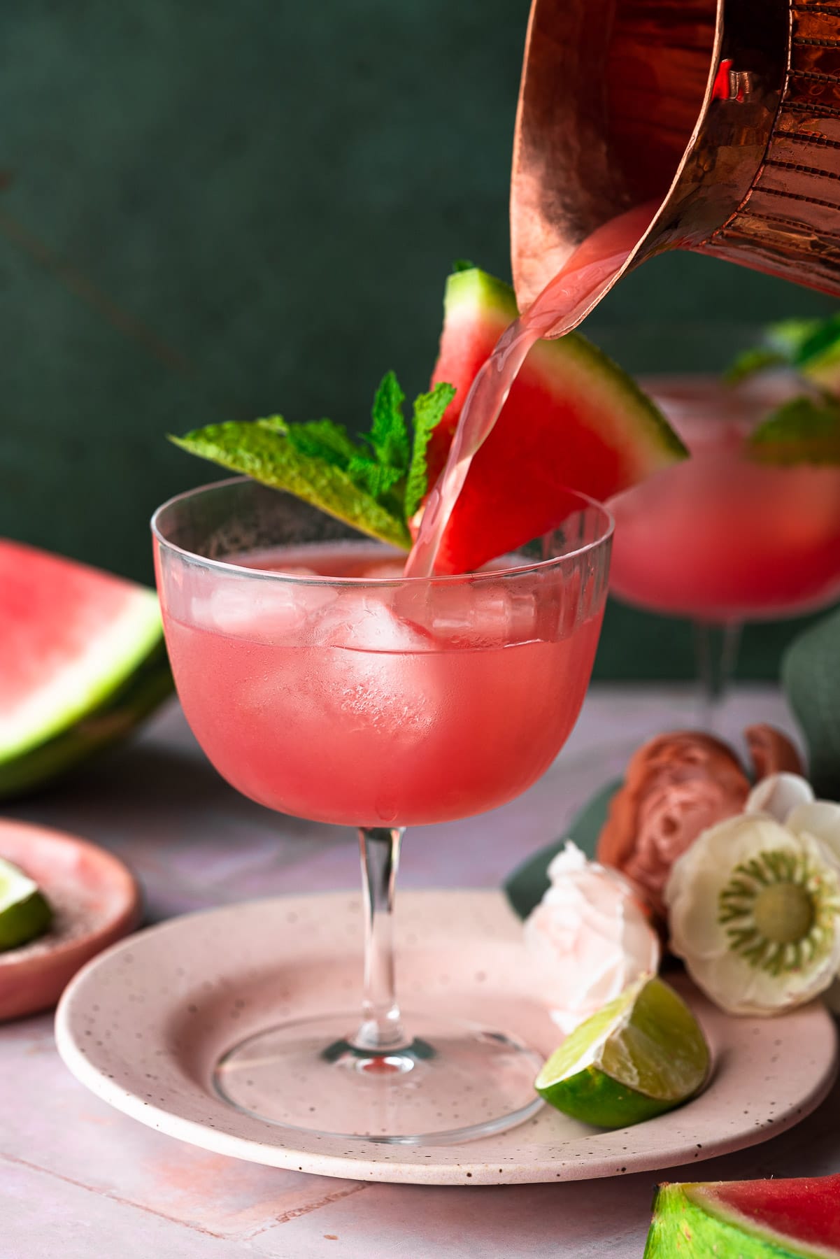 pouring fresh watermelon juice into a coupe from a copper pitcher