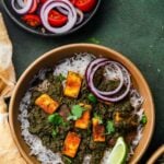 a bowl of swiss chard saag paneer with tomato onion salad for pinterest