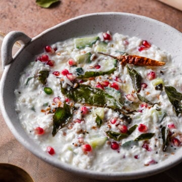 macro shot of curd rice in a white bowl with curry leaves and pomgranates