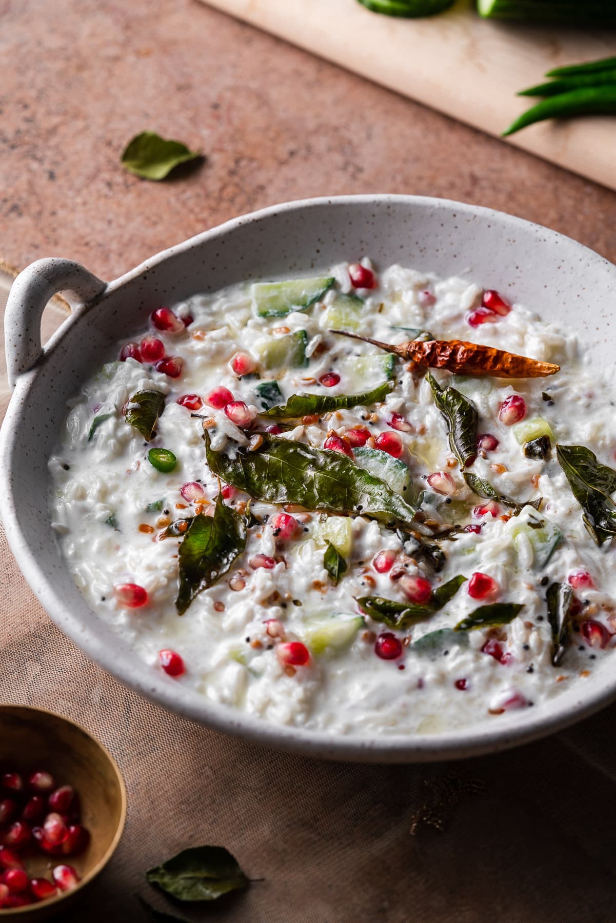 macro shot of curd rice in a white bowl with curry leaves and pomgranates