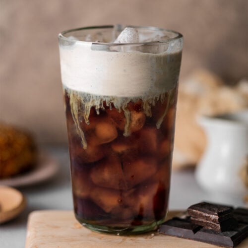 a glass of chocolate cream cold brew on a wooden board with chocolate pieces