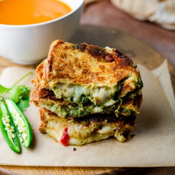 stack of chutney grilled cheese sandwiches with tomato soup on a wooden board.