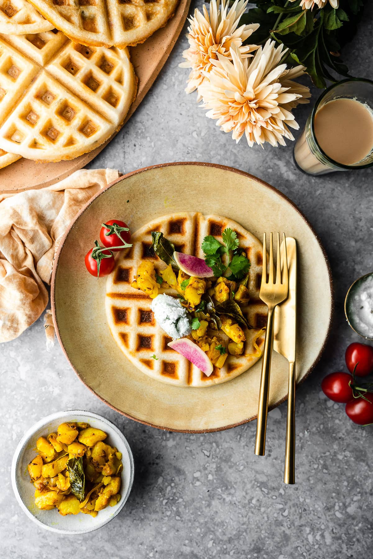 dosa waffle in a plate with aloo, chutney, and tomatoes with a platter of waffles and chai.