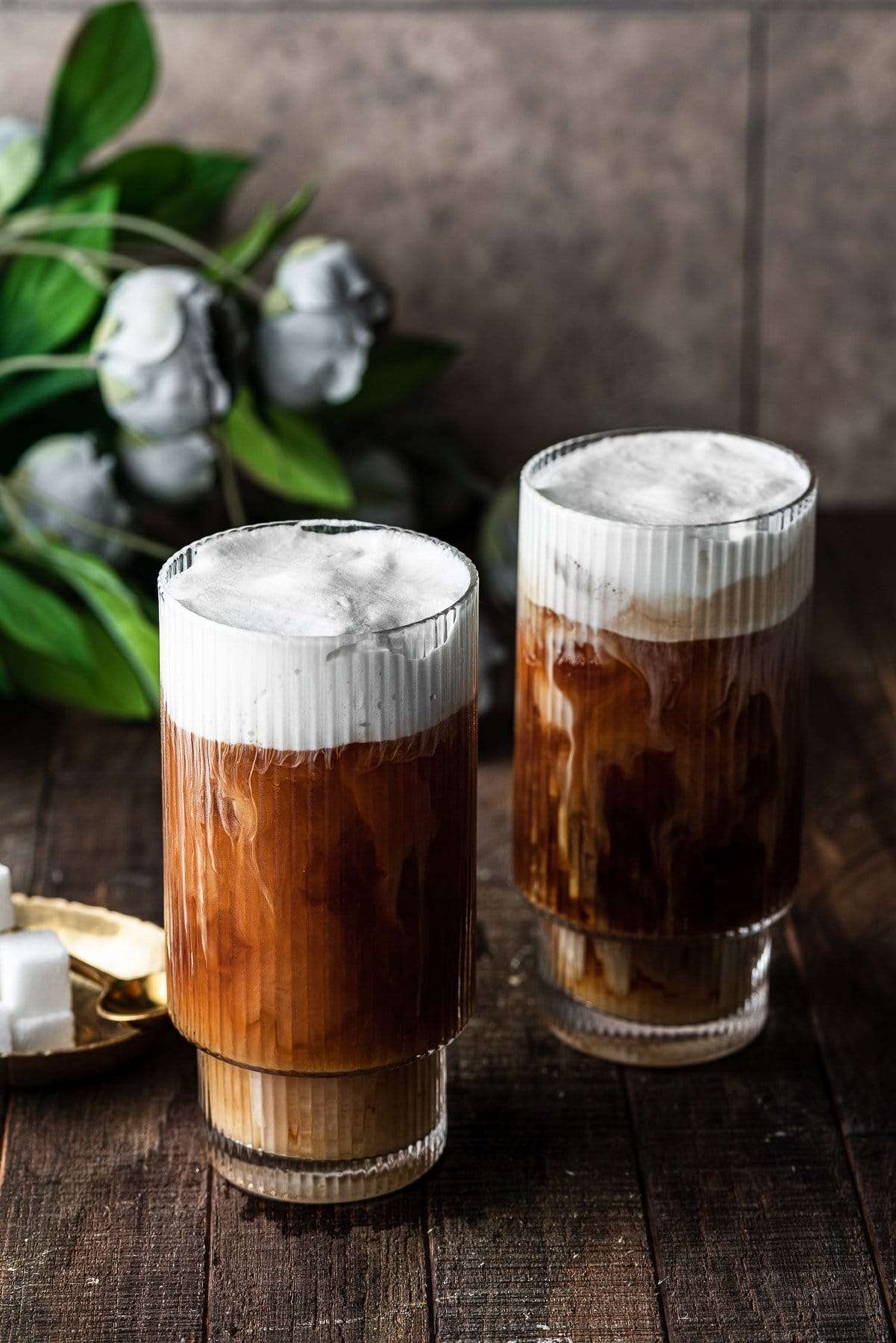 two glasses of coffee with cold foam on top of both of them and the milk cascading down.