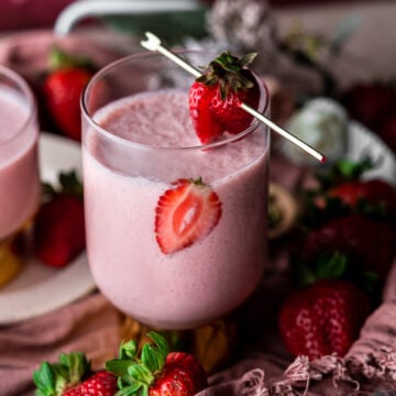 Glass of strawberry lassi in a tray with fresh strawberries.