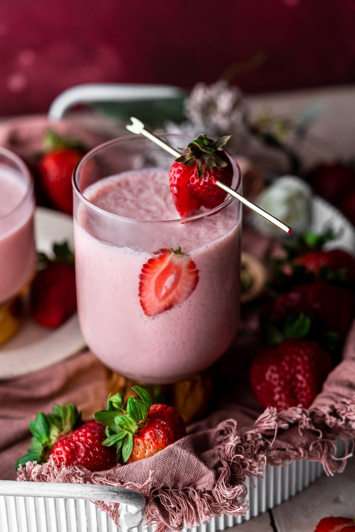 Glass of strawberry lassi in a tray with fresh strawberries.