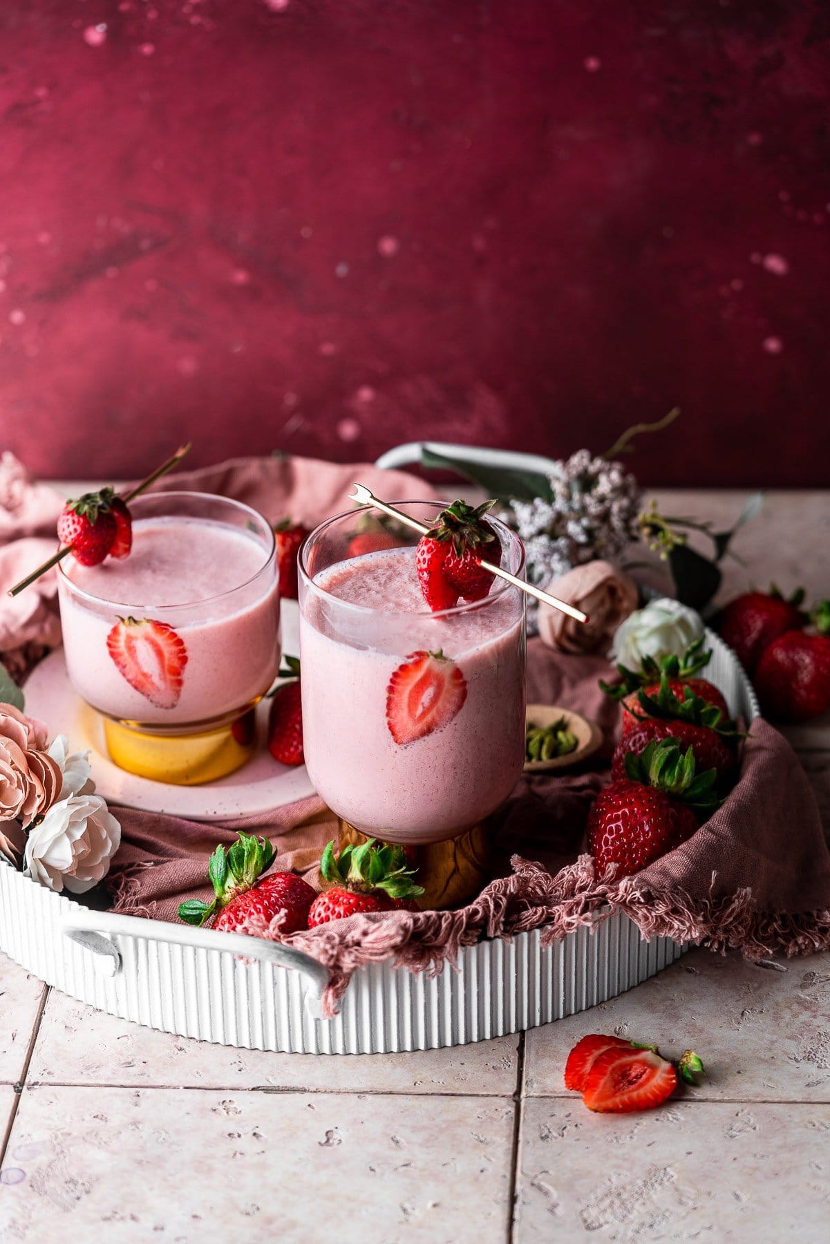 Two Strawberry Lassis in a tray decorated with fresh strawberries and flowers.