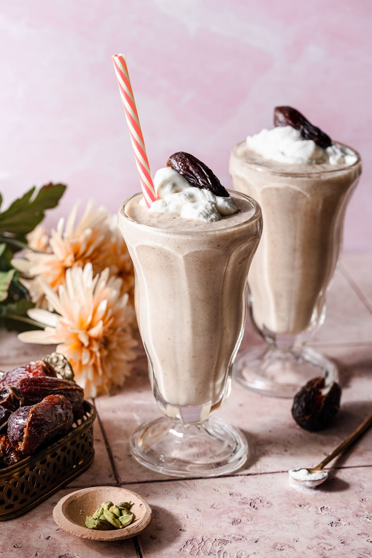 Two date shakes in milkshake glasses with whipped cream, a date, and a straw.