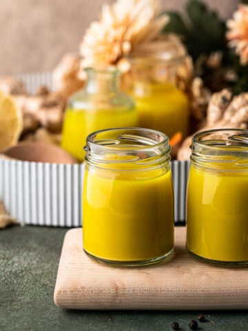 Two small jars of ginger turmeric shots on a wooden board.