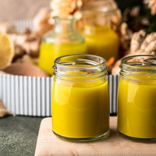 Two small jars of ginger turmeric shots on a wooden board.
