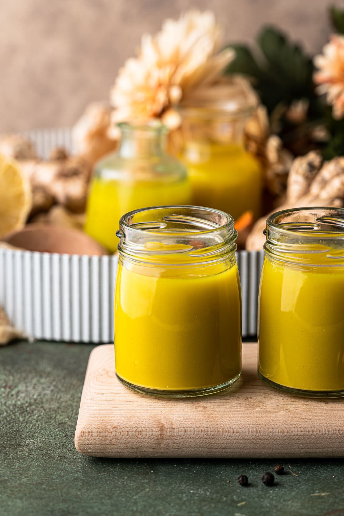 Two small jars of ginger turmeric shots on a wooden board.