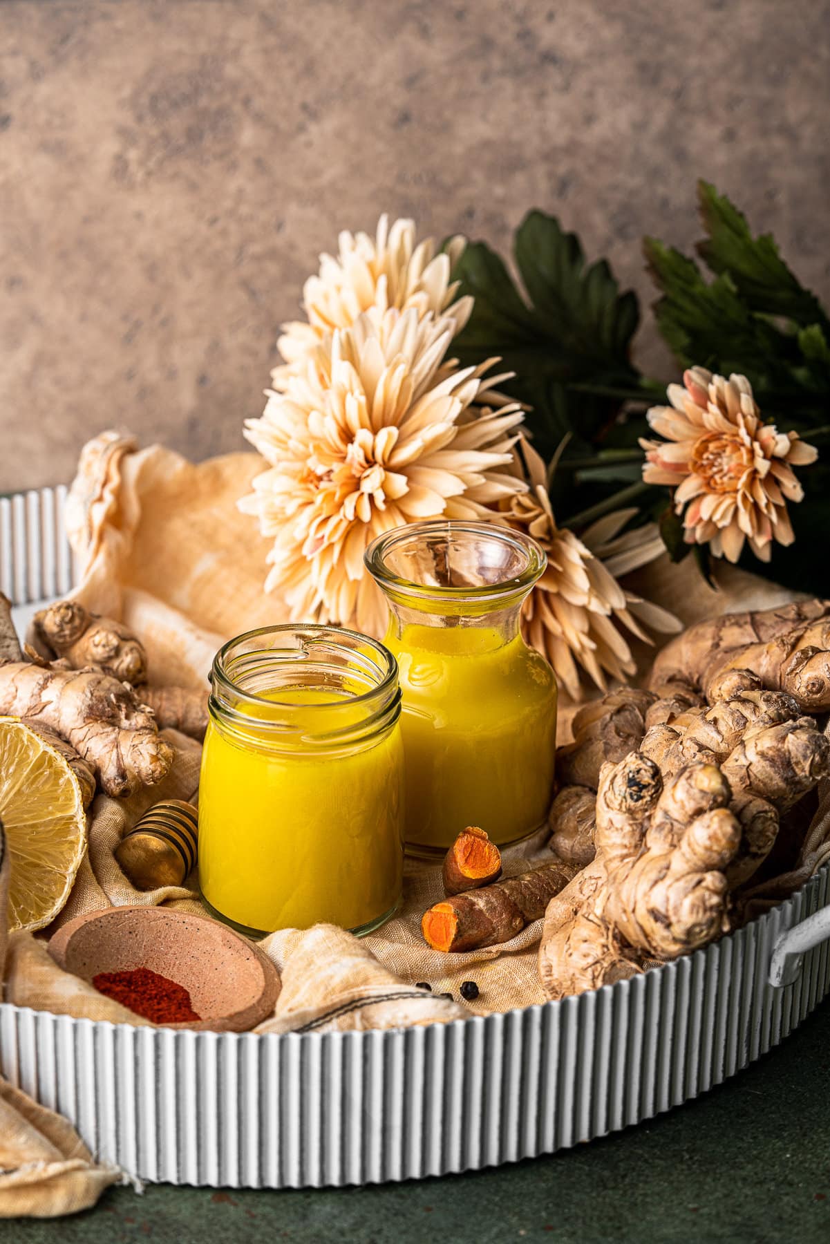 Two jars of ginger turmeric shots in a tray with all of the ingredients and flowers.