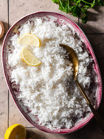 basmati rice in a platter with lemon slices and a gold spoon.