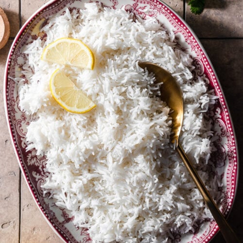 basmati rice in a platter with lemon slices and a gold spoon.