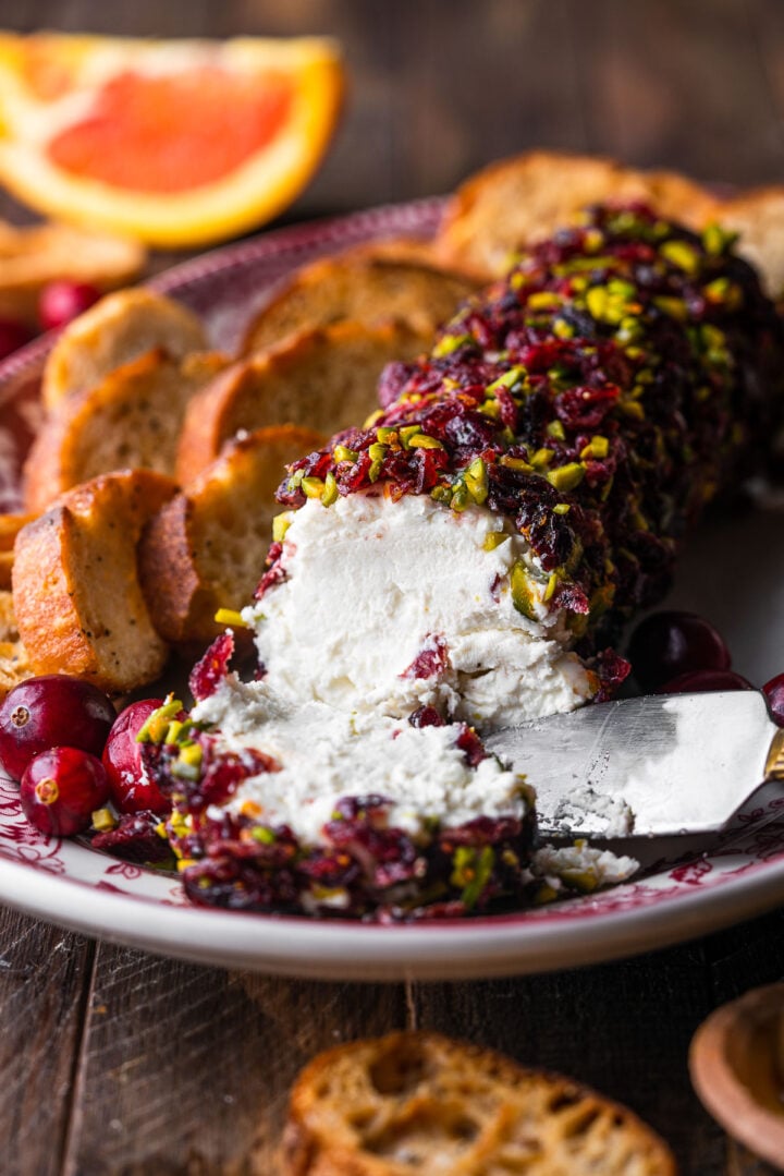 Cranberry Pistachio Goat Cheese log on a platter with crostinis and fresh cranberries.