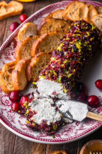 Cranberry Pistachio Goat Cheese log on a platter with crostinis and fresh cranberries.