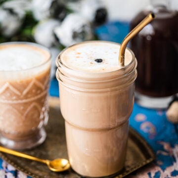 Two cups of dirty chai in a platter with a gold straw and spoon.