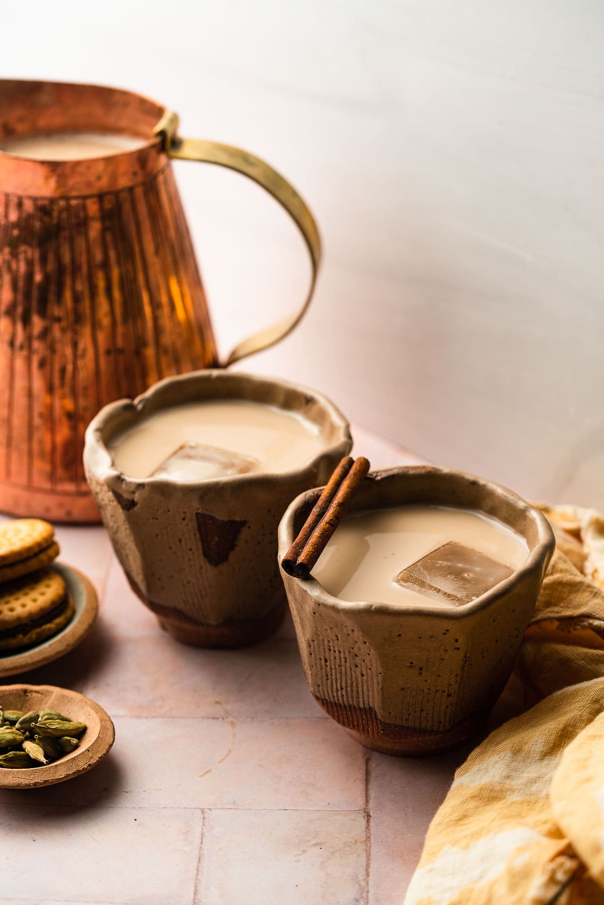 Two cups of chai horchata with a cinnamon stick to garnish with a pitcher of chai horchata.