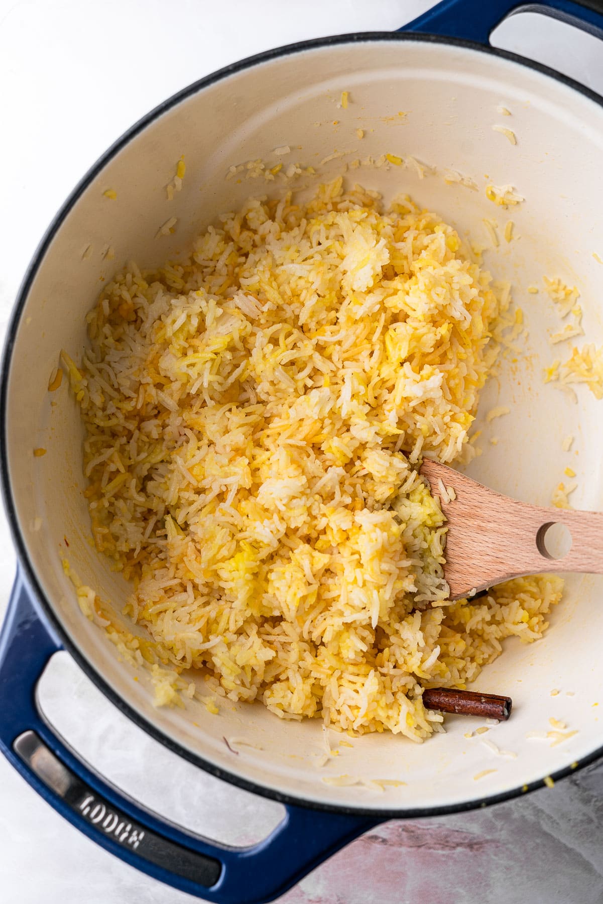 Saffron Rice fluffed with a wooden spoon in a Lodge Pot.