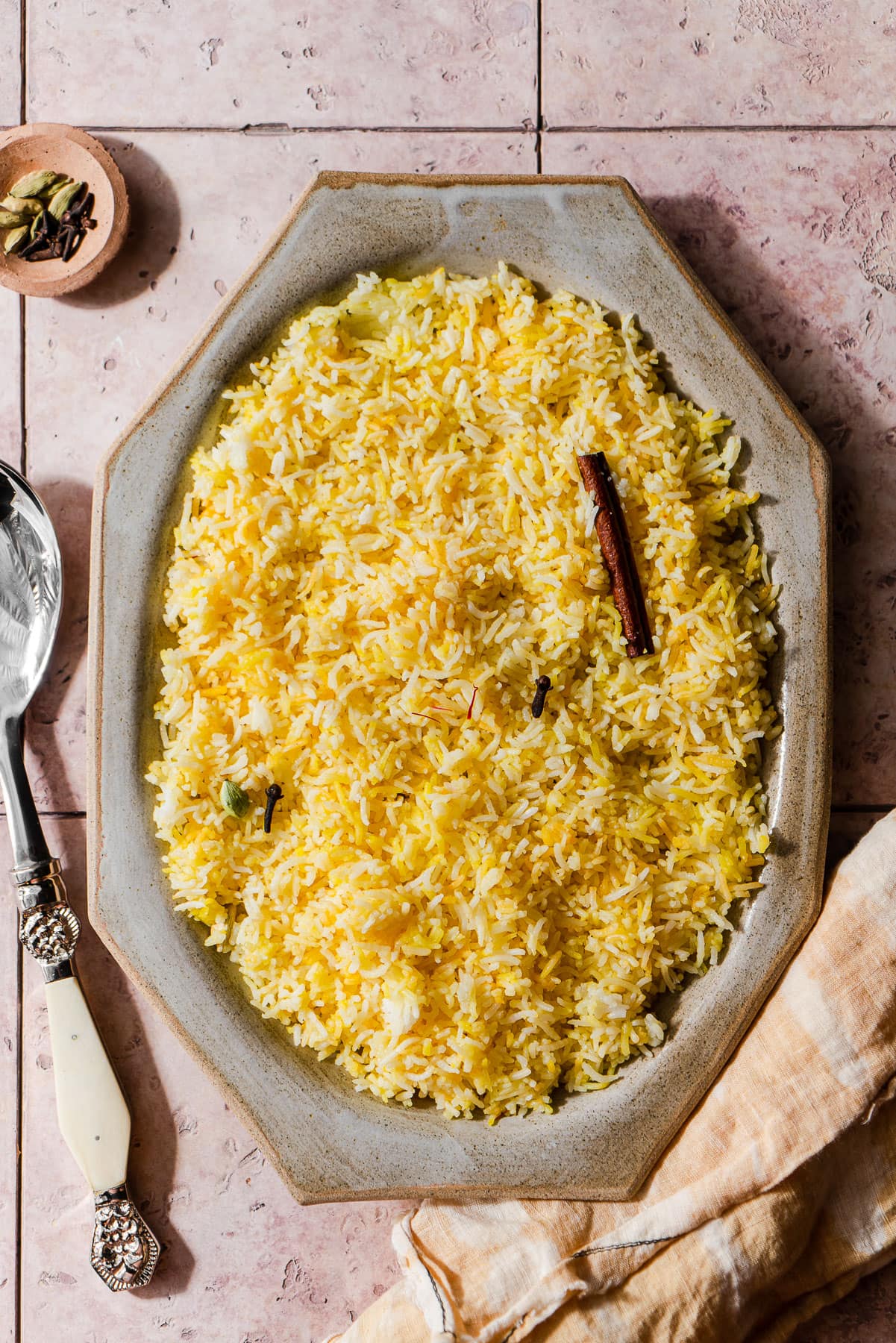 Indian Saffron rice in a platter with spices and a serving spoon.
