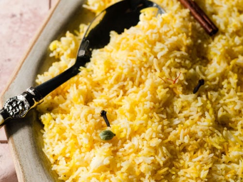 Platter of saffron rice with spices and a serving spoon.