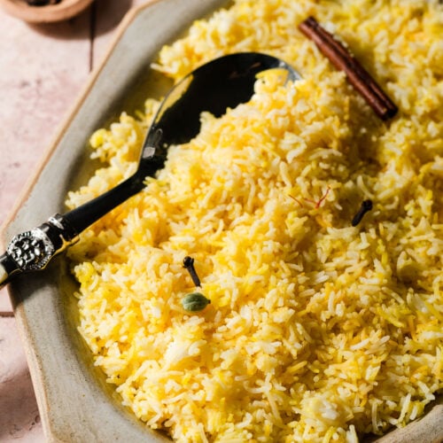 Platter of saffron rice with spices and a serving spoon.