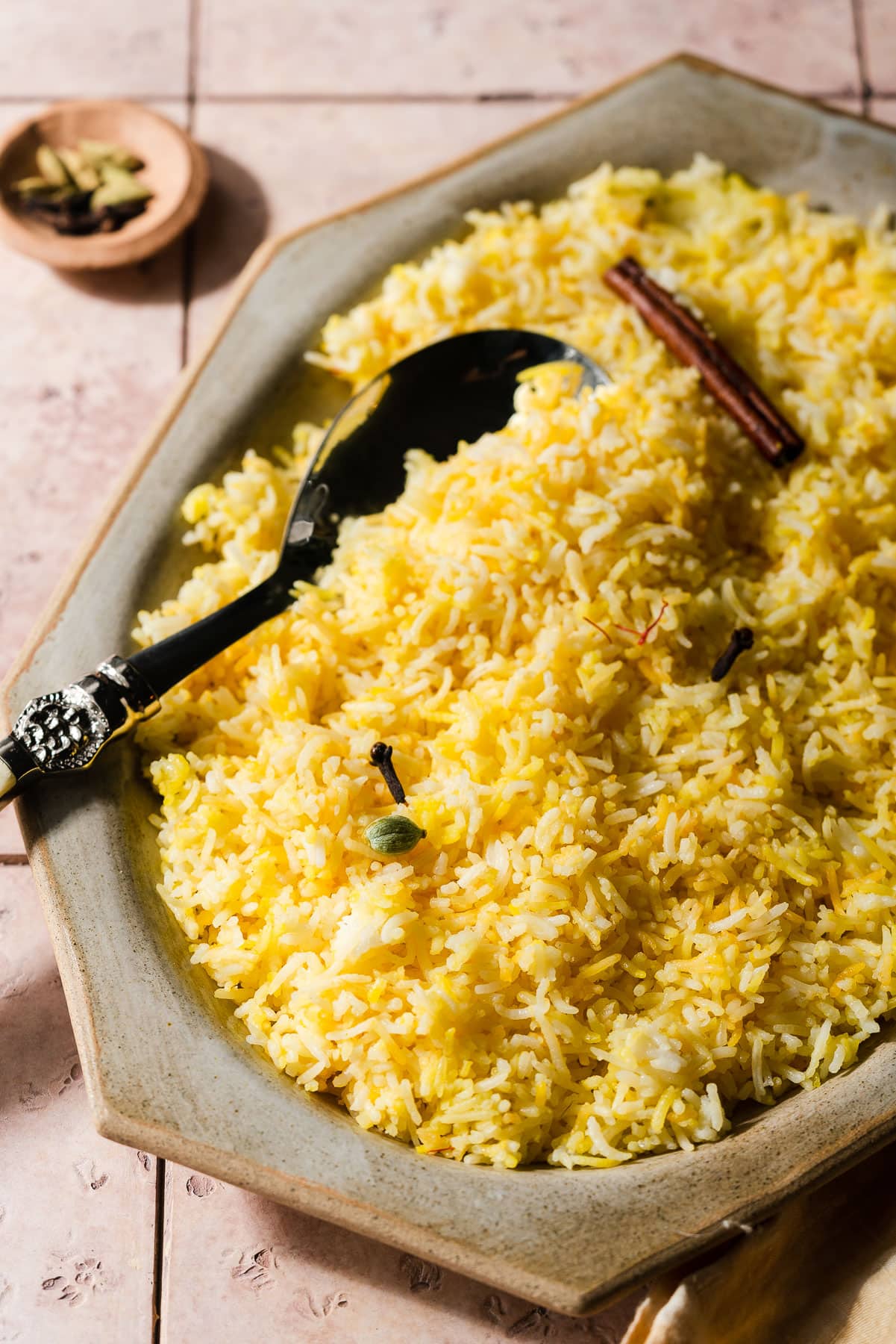 Platter of saffron rice with spices and a serving spoon.