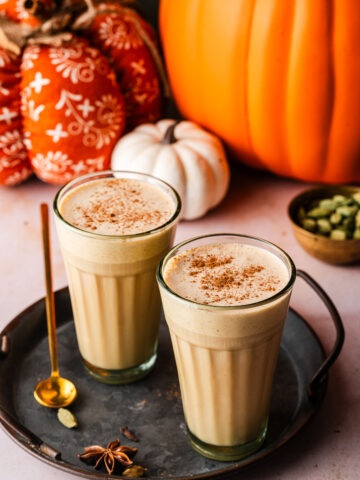 Two Pumpkin Cream Chai Lattes in platter surrounded by spices and pumpkins.
