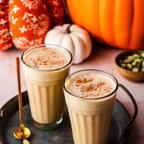 Two Pumpkin Cream Chai Lattes in platter surrounded by spices and pumpkins.