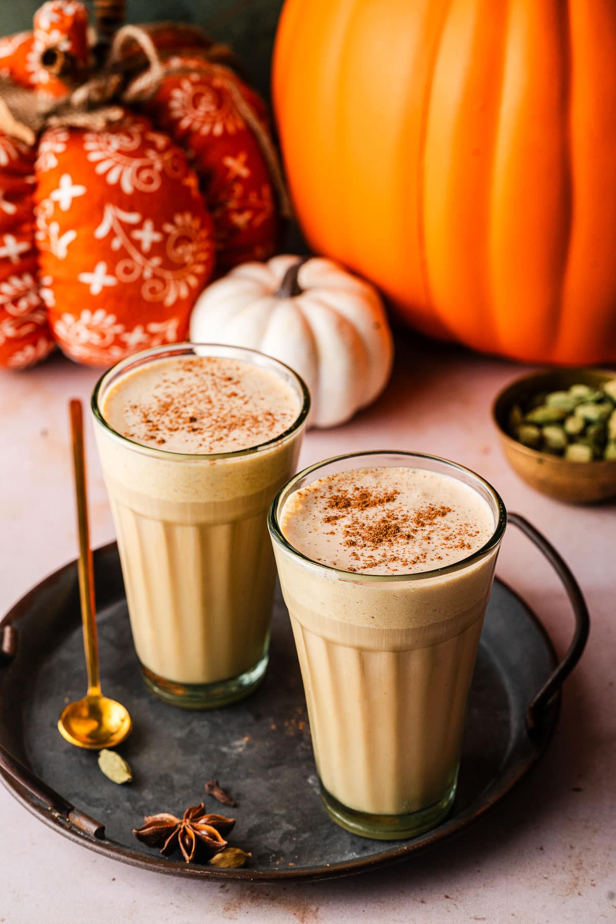 Two Pumpkin Cream Chai Lattes in platter surrounded by spices and pumpkins.