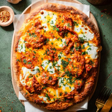 Butter Chicken Garlic Naan Pizza in a serving tray with cloves and a head of garlic, chili falkes, and a fork and knife.