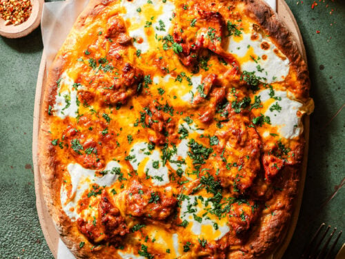 Butter Chicken Garlic Naan Pizza in a serving tray with cloves and a head of garlic, chili falkes, and a fork and knife.