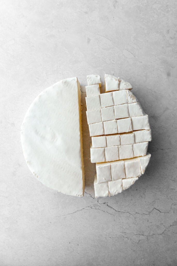 A wheel of brie with half of it cubed.