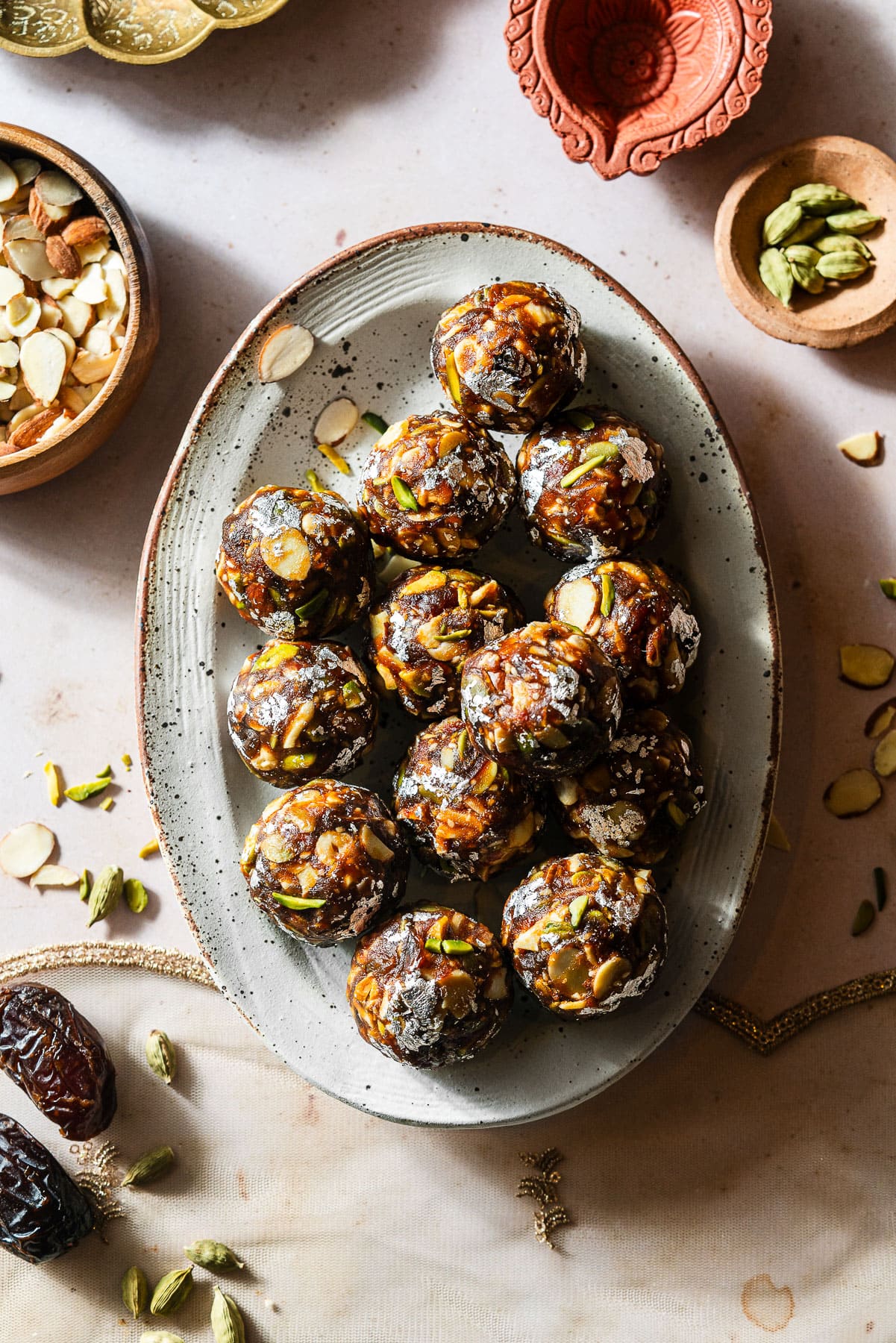 A dozen date nut ladoos in a platter surrounded by ingredients and a diya.