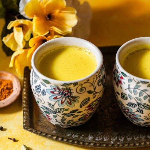 Two cups of haldi doodh in kulhads in a platter with whole spices and flowers.