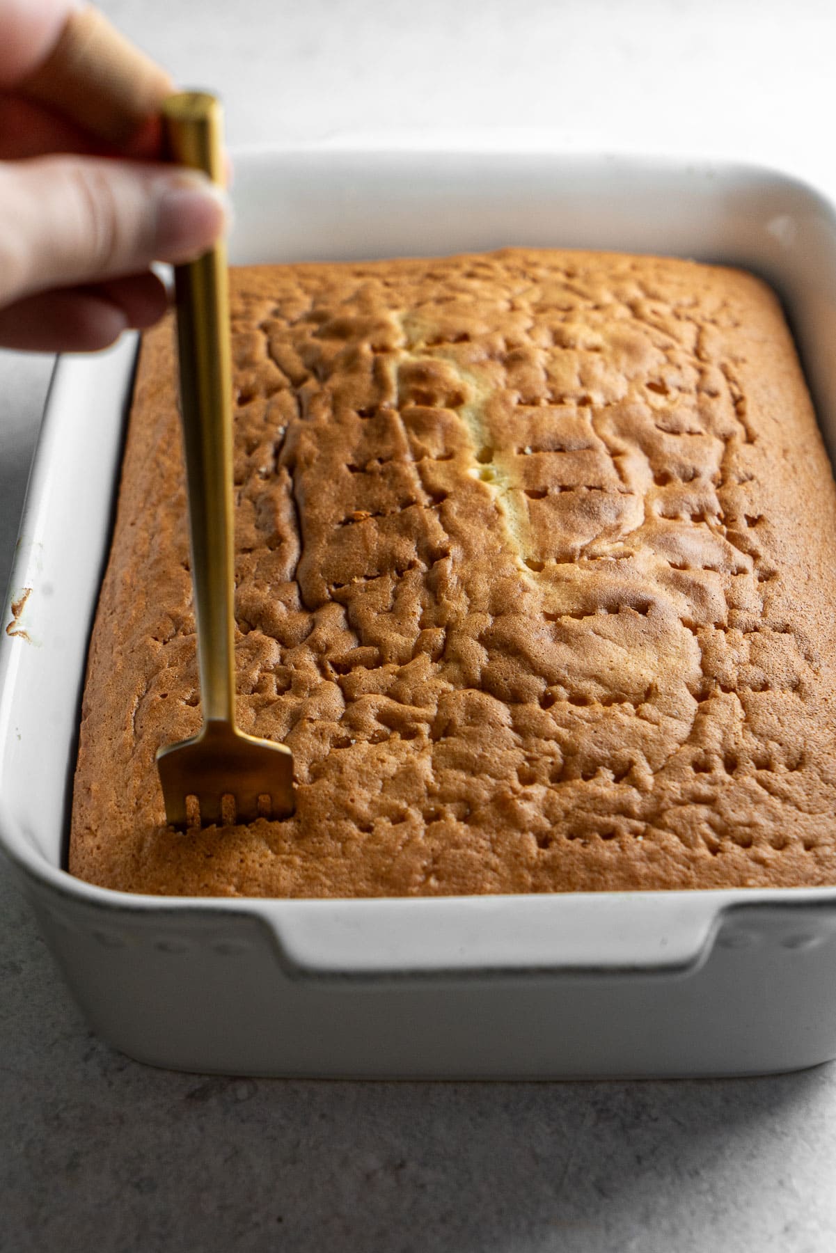 A fork poking holes into a baked cake in a baking dish.