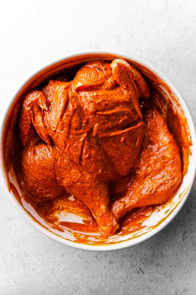 Spatchcocked tandoori chicken marinated in a bowl.