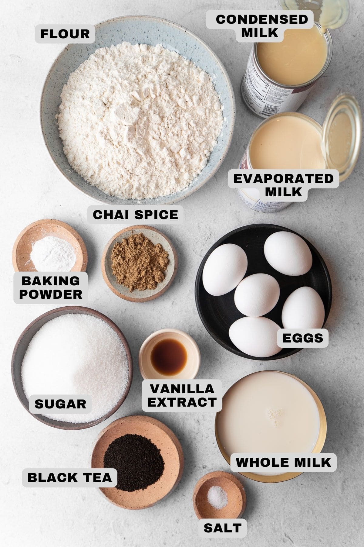 Flour, condensed milk, evaporated milk, chai spice, baking powder, eggs, vanilla extract, sugar, black tea, salt, whole milk ingredients with labels.