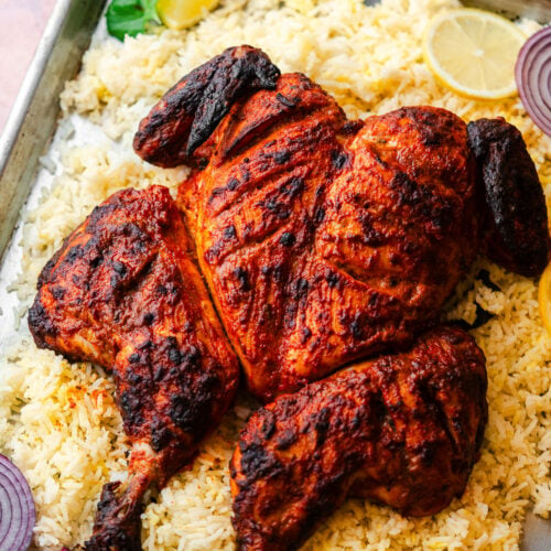 Roasted Spatchcock Tandoori Chicken in a baking tray with rice, onion, lemons, and raita.