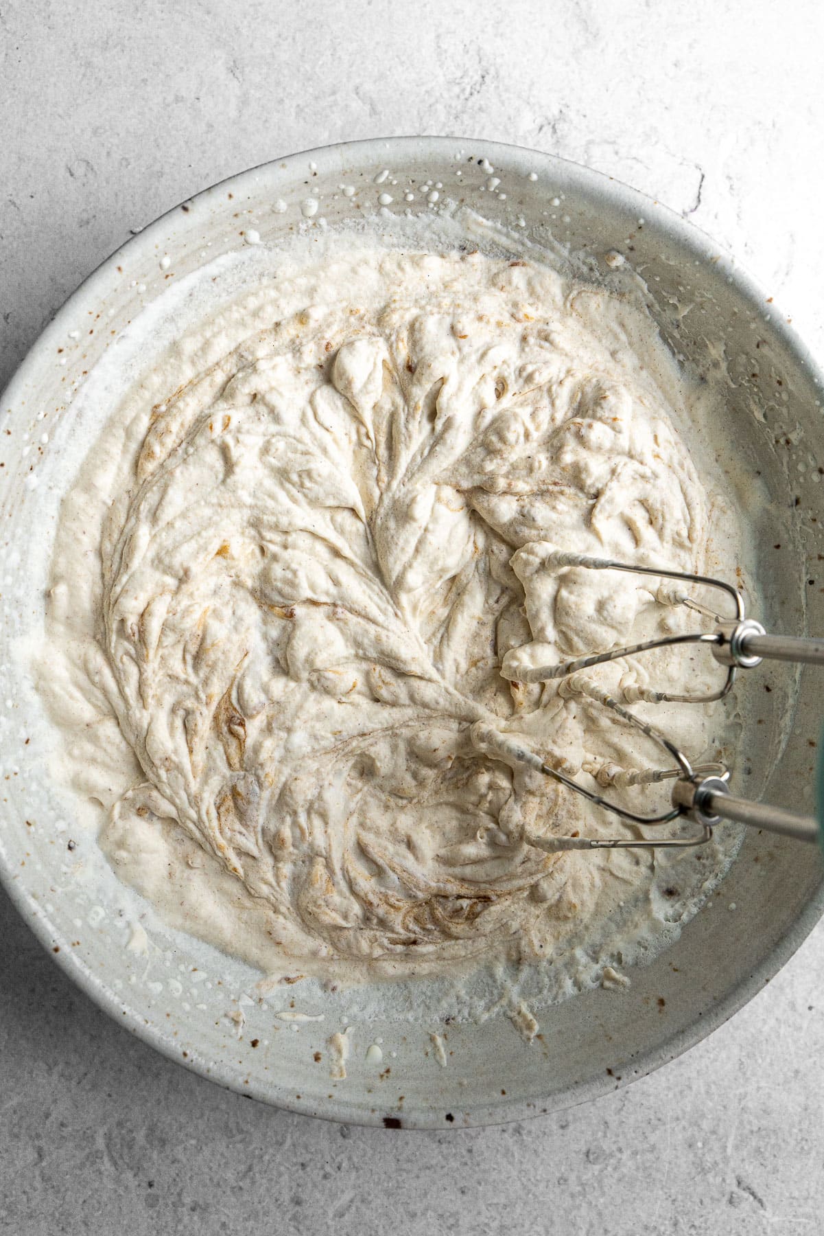 A handheld electric mixer beating whipped cream with chai date caramel.