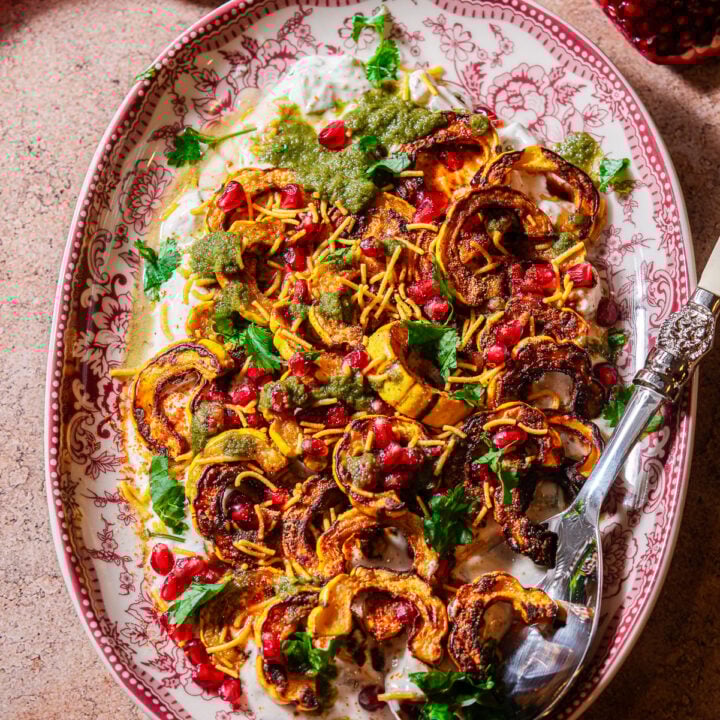 A serving platter filled with roasted delicata squash chaat with a serving spoon.